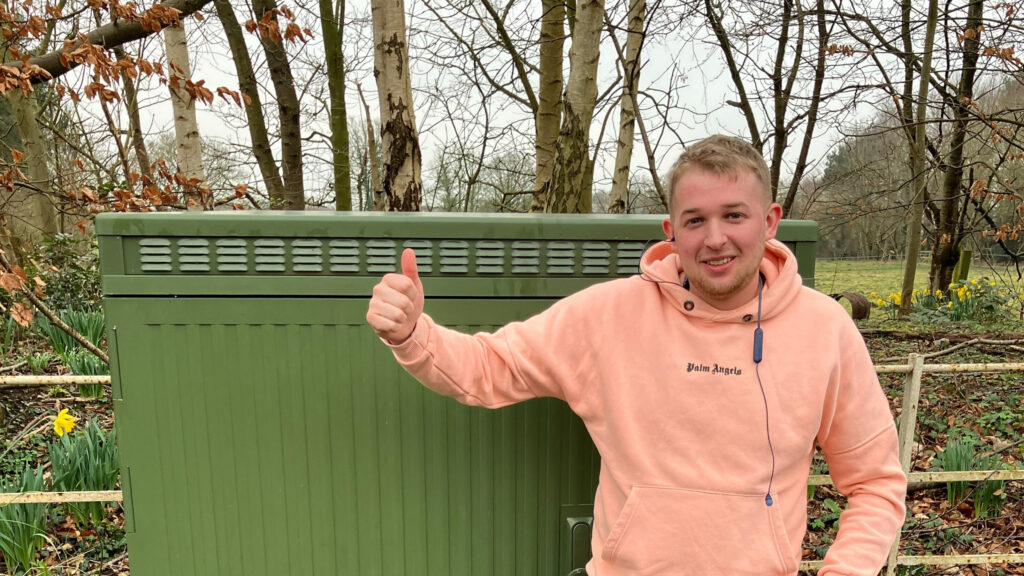 Young man wearing peach hoodie poses with thumbs up in front of green full fibre cabinet in Escrick