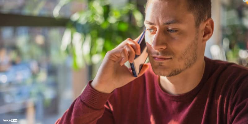 Man holding phone up to ear looking out a window on a scam call